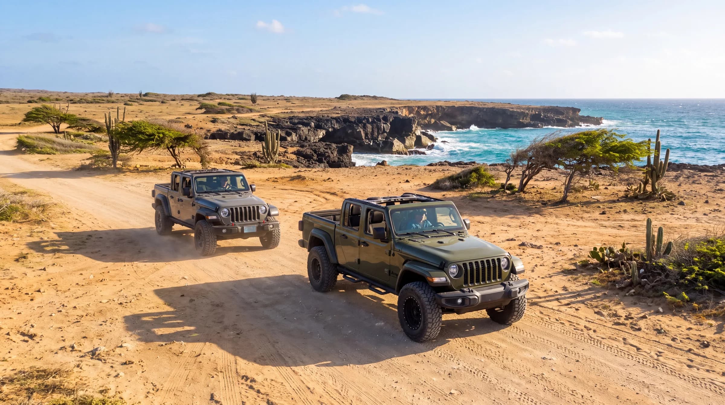 Two Jeeps with the tops off driving up a sandy coastal track toward the camera, turquoise sea behind