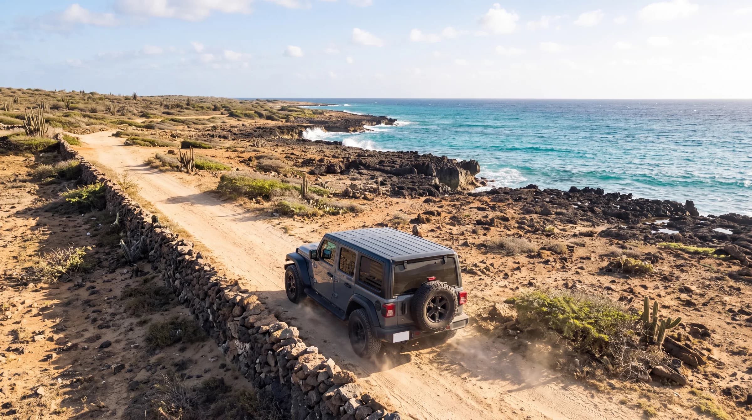 Gray four-door Jeep Wrangler seen from behind on the stone-walled coastal trail in Aruba