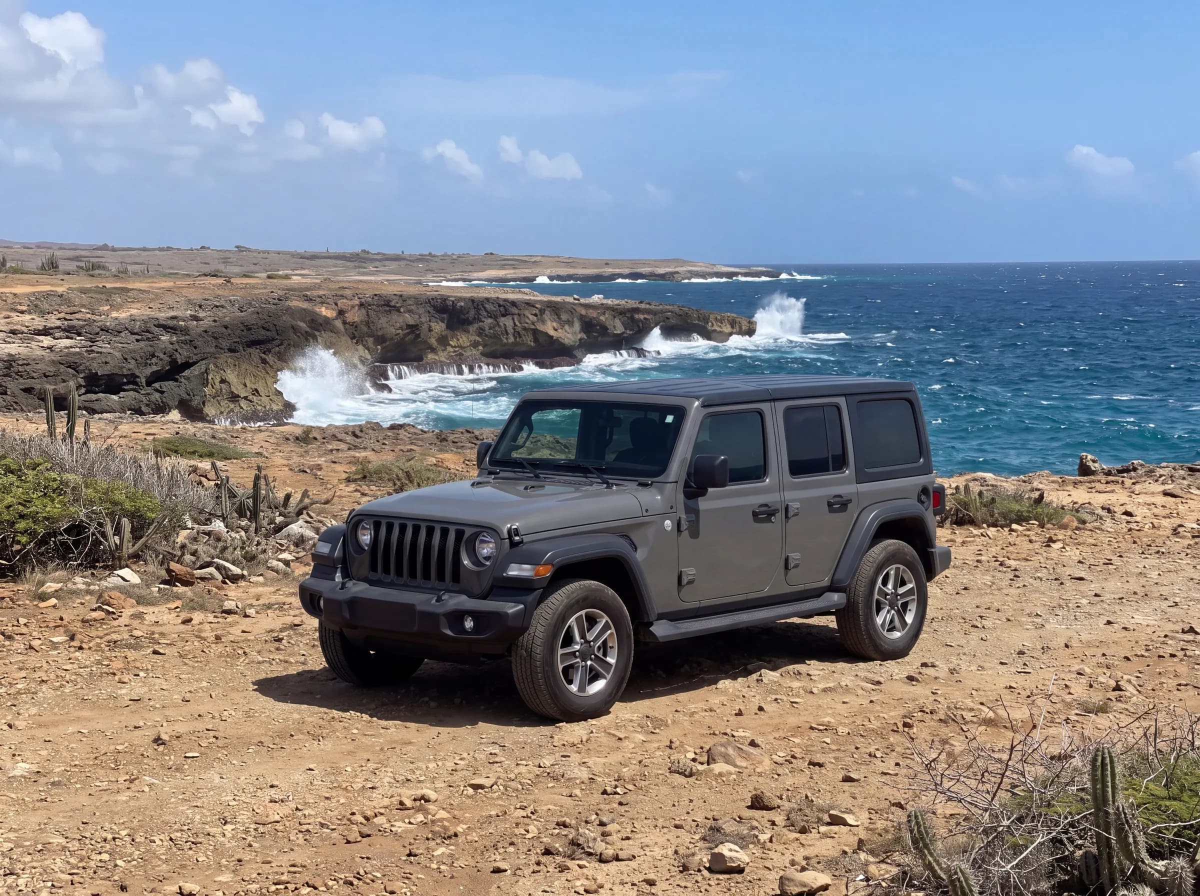 Gray four-door Jeep Wrangler parked on a rocky pull-off above the surf on the Aruba north coast